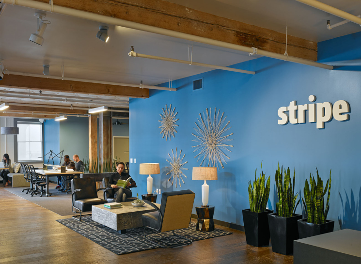 A lounge area inside a Stripe office, with a blue accent wall and the Stripe logo.
